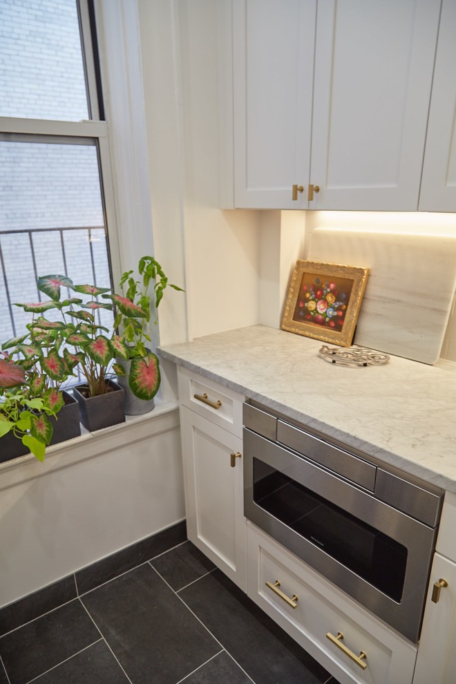 This is an example of a mid-sized transitional galley separate kitchen in New York with a farmhouse sink, white cabinets, white splashback, stainless steel appliances, shaker cabinets, quartz benchtops, ceramic splashback, cement tiles, grey floor and grey benchtop.