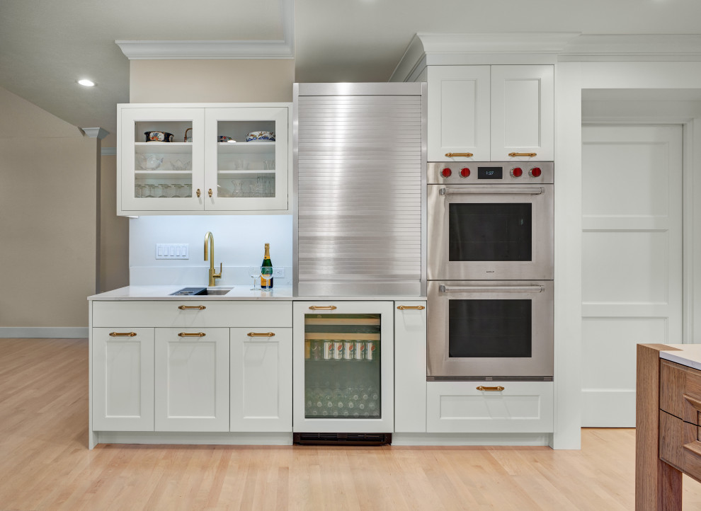 Large u-shaped light wood floor, brown floor and tray ceiling open concept kitchen photo in Sacramento with an undermount sink, shaker cabinets, white cabinets, quartz countertops, white backsplash, stone tile backsplash, stainless steel appliances, an island and white countertops