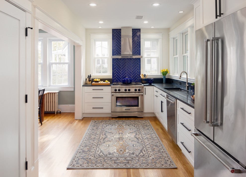 This is an example of a large transitional l-shaped eat-in kitchen in DC Metro with shaker cabinets, white cabinets, granite benchtops, blue splashback, stainless steel appliances, black benchtop, an undermount sink, ceramic splashback, medium hardwood floors, no island and brown floor.