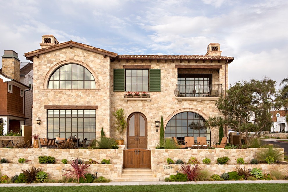 Inspiration for a large mediterranean two-storey beige house exterior in Orange County with stone veneer, a tile roof and a gable roof.