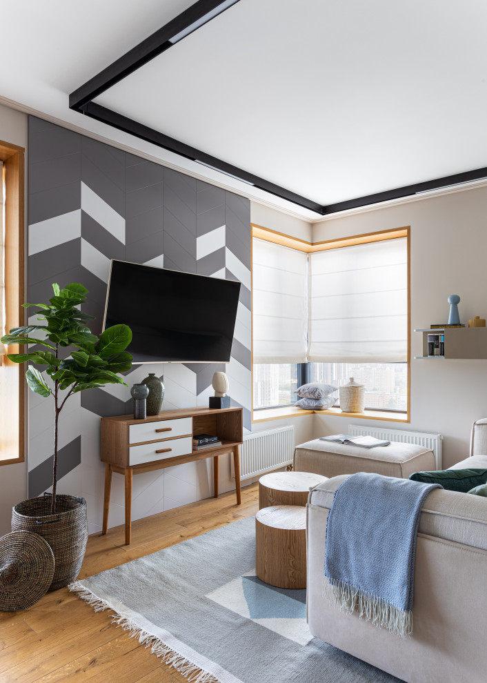 На фото: серо-белая гостиная комната в скандинавском стиле с серыми стенами, паркетным полом среднего тона и телевизором на стене с
