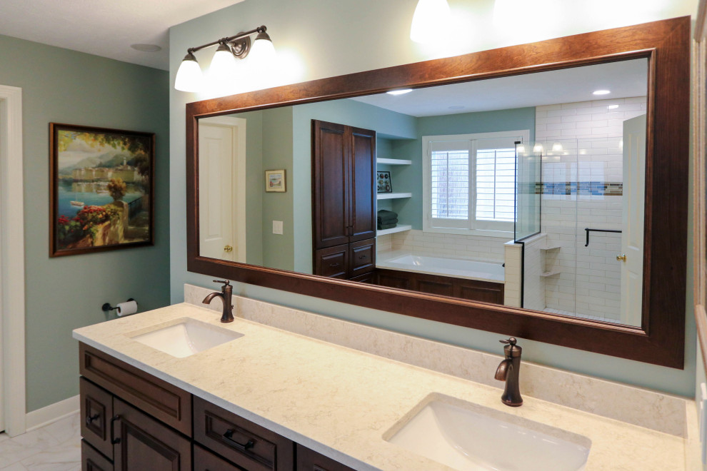 Photo of a mid-sized traditional master bathroom in Cleveland with raised-panel cabinets, brown cabinets, a drop-in tub, a corner shower, a two-piece toilet, white tile, porcelain tile, green walls, cement tiles, an undermount sink, engineered quartz benchtops, beige floor, a hinged shower door, beige benchtops, a double vanity and a freestanding vanity.