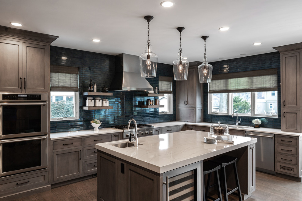 Photo of a large country l-shaped eat-in kitchen in Chicago with a single-bowl sink, medium wood cabinets, quartz benchtops, blue splashback, stainless steel appliances, medium hardwood floors, with island, brown floor, grey benchtop, recessed-panel cabinets and cement tile splashback.