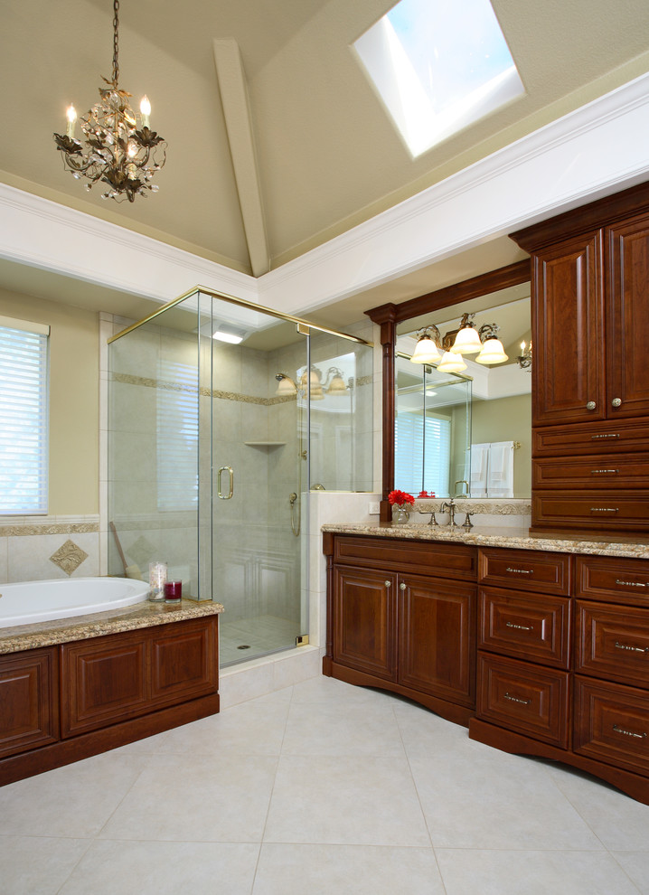Mid-sized traditional bathroom in Other with furniture-like cabinets, brown cabinets, a drop-in tub, a corner shower, a two-piece toilet, beige walls, ceramic floors, an undermount sink, granite benchtops, grey floor, a hinged shower door and beige benchtops.