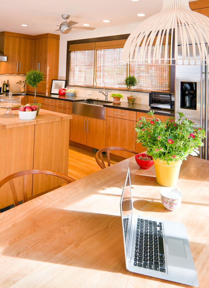 This is an example of a midcentury kitchen in Boston with stainless steel appliances, a farmhouse sink, flat-panel cabinets, medium wood cabinets and wood benchtops.