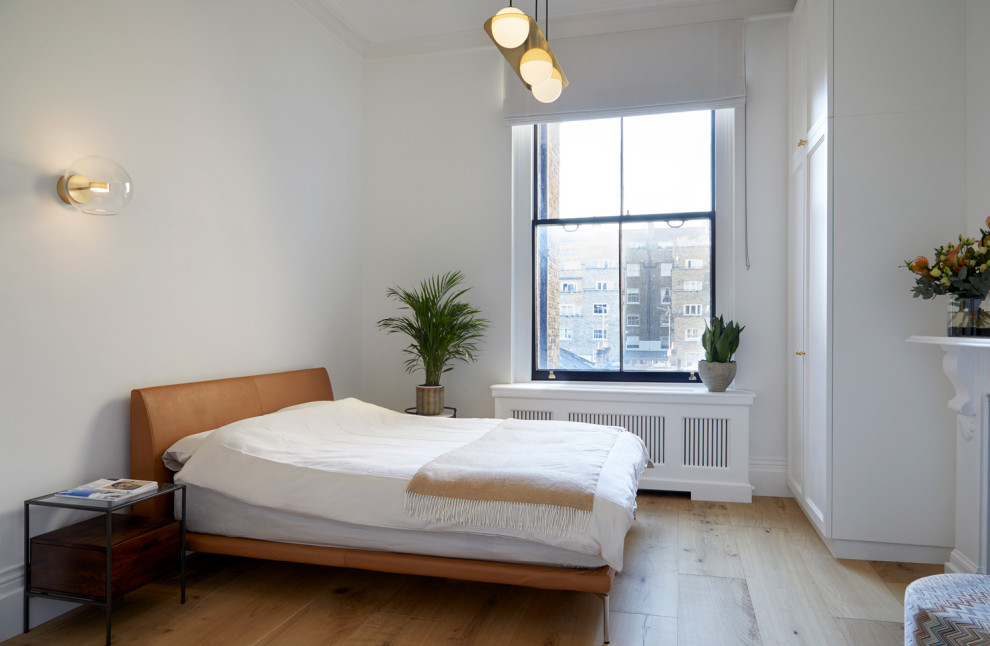 Imagen de dormitorio principal escandinavo de tamaño medio con paredes blancas, suelo de madera clara, todas las chimeneas, marco de chimenea de yeso y suelo beige