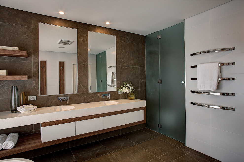 Inspiration for a large contemporary master bathroom in Other with flat-panel cabinets, white cabinets, a freestanding tub, brown tile, an integrated sink, a wall-mount toilet, porcelain tile, white walls, porcelain floors and engineered quartz benchtops.