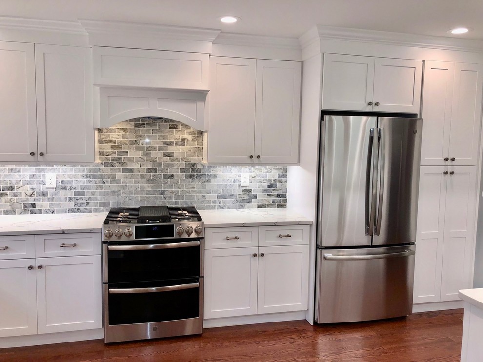 Example of a mid-sized transitional u-shaped dark wood floor and brown floor enclosed kitchen design with an undermount sink, shaker cabinets, white cabinets, marble countertops, gray backsplash, stone tile backsplash, stainless steel appliances, no island and white countertops