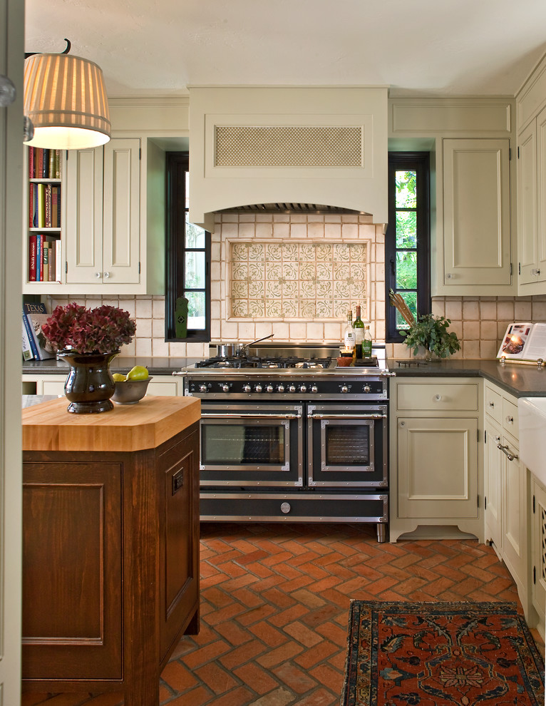 Traditional kitchen in Dallas with beige cabinets, black appliances and brick floors.