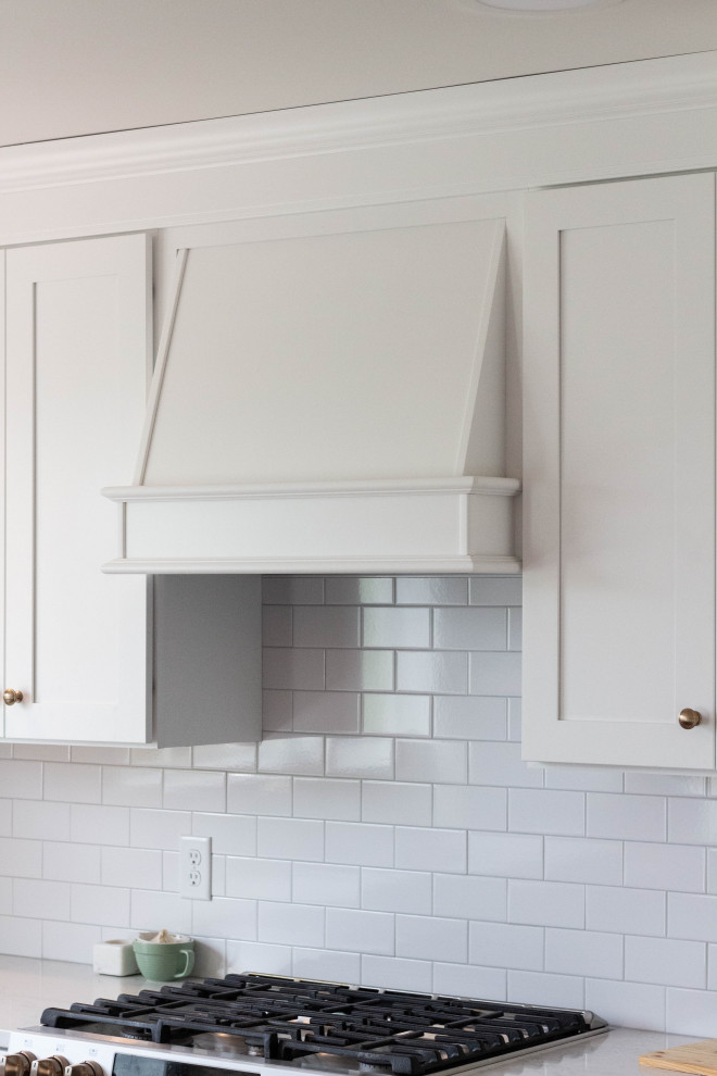 Open concept kitchen - mid-sized transitional l-shaped medium tone wood floor and brown floor open concept kitchen idea with an undermount sink, shaker cabinets, white cabinets, quartzite countertops, white backsplash, ceramic backsplash, white appliances, an island and white countertops