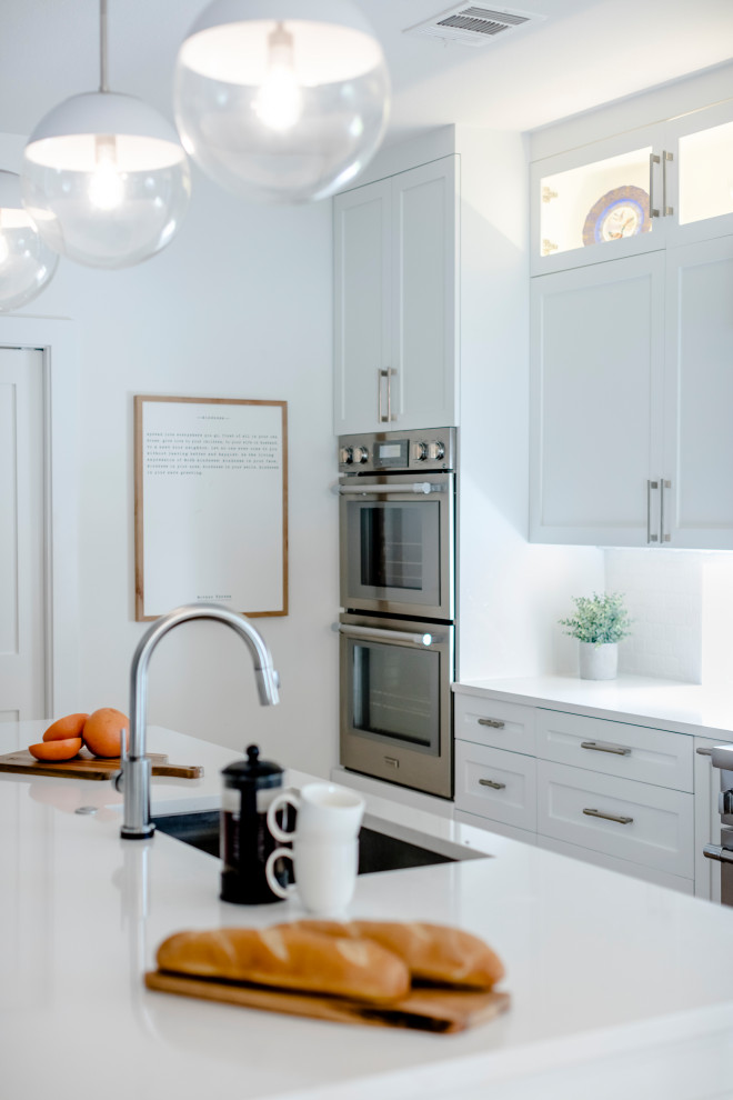 Example of a large transitional l-shaped light wood floor and brown floor eat-in kitchen design in Austin with a single-bowl sink, shaker cabinets, white cabinets, quartz countertops, white backsplash, ceramic backsplash, stainless steel appliances, an island and white countertops