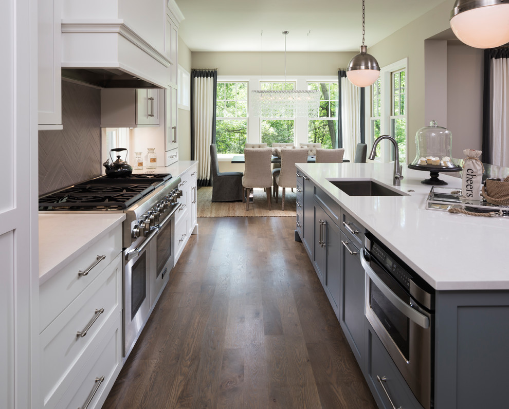 Eat-in kitchen - mid-sized transitional galley medium tone wood floor eat-in kitchen idea in Minneapolis with an undermount sink, shaker cabinets, white cabinets, gray backsplash, stainless steel appliances and an island