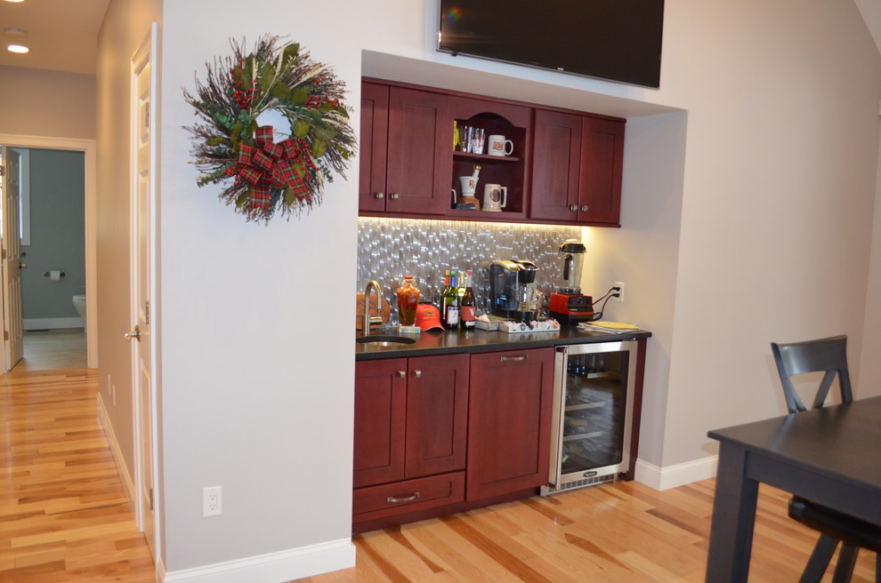 This is an example of a small transitional single-wall wet bar in Boston with an undermount sink, shaker cabinets, red cabinets, grey splashback, light hardwood floors, brown floor and metal splashback.