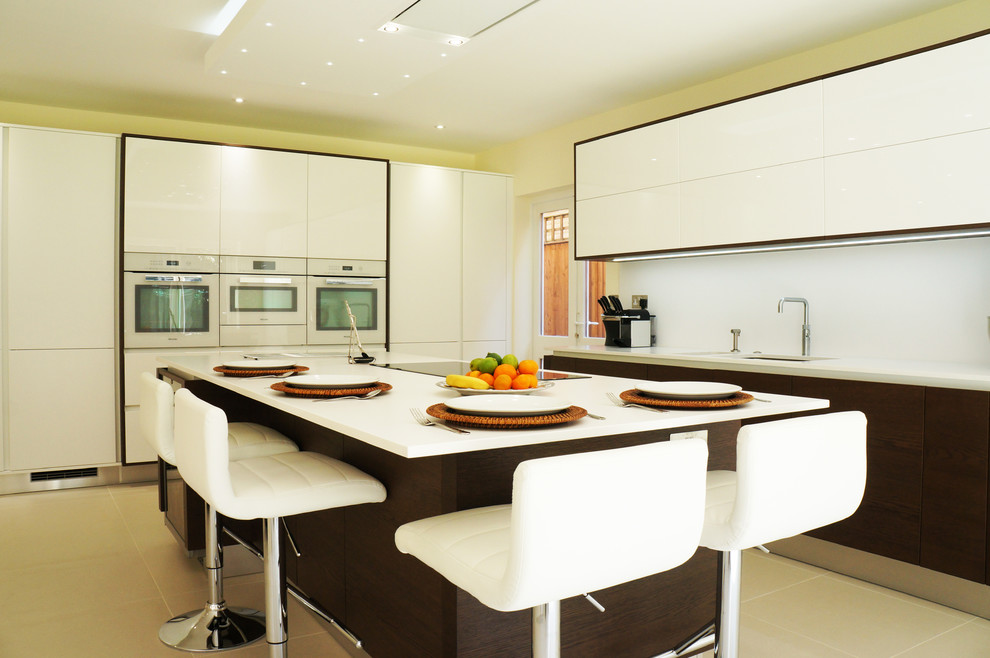 Large midcentury u-shaped eat-in kitchen in Surrey with a drop-in sink, flat-panel cabinets, white cabinets, solid surface benchtops, white splashback, ceramic splashback, stainless steel appliances, ceramic floors and a peninsula.