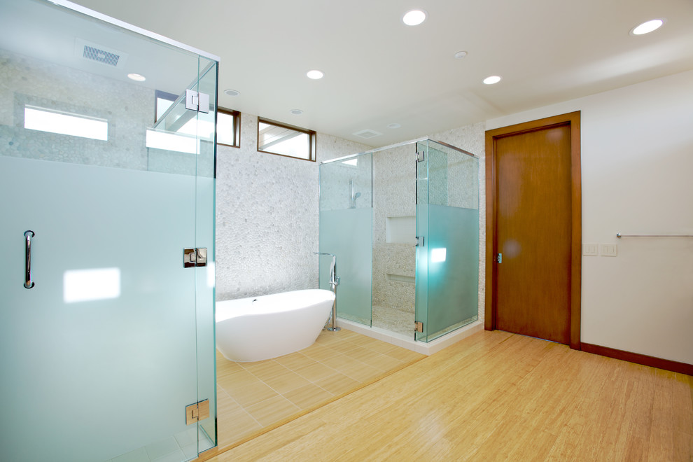 This is an example of an expansive contemporary master bathroom in Orange County with a freestanding tub, a corner shower, white tile, white walls, light hardwood floors, pebble tile and a one-piece toilet.