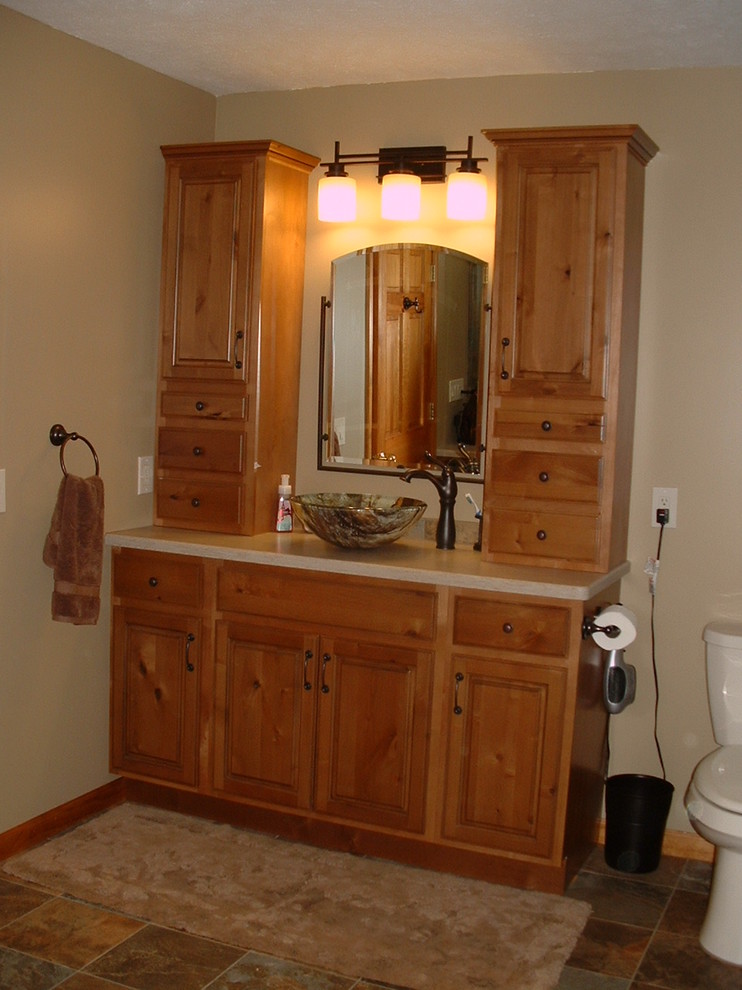 Photo of a country bathroom in Other with a console sink, raised-panel cabinets, medium wood cabinets, solid surface benchtops, a corner shower, multi-coloured tile and porcelain tile.
