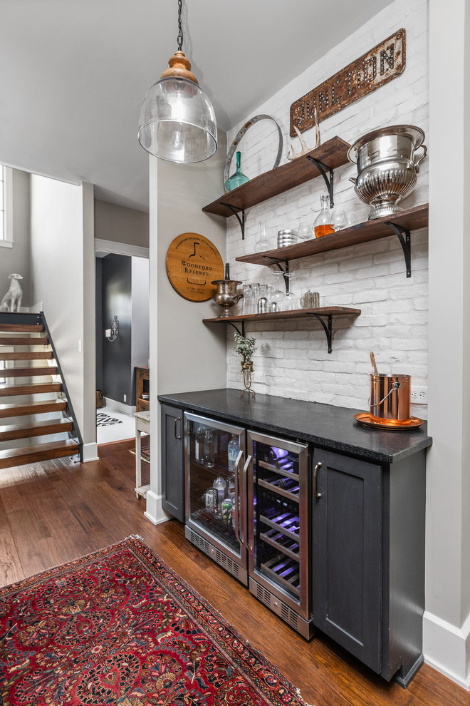 Inspiration for a small country single-wall home bar in Indianapolis with no sink, shaker cabinets, black cabinets, white splashback, brick splashback, dark hardwood floors and black benchtop.