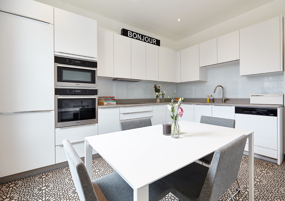 Contemporary l-shaped eat-in kitchen in London with an undermount sink, flat-panel cabinets, white cabinets, white splashback, glass sheet splashback, panelled appliances, cement tiles, no island and multi-coloured floor.