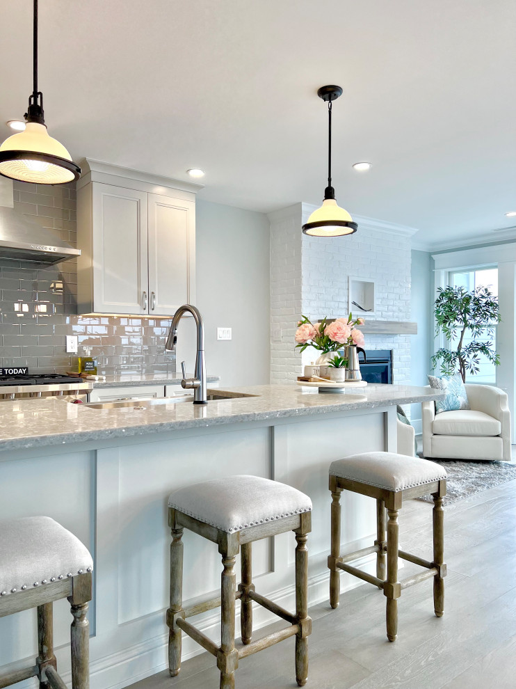 Inspiration for a beach style kitchen in Other with an undermount sink, recessed-panel cabinets, grey cabinets, granite benchtops, grey splashback, ceramic splashback, stainless steel appliances, light hardwood floors, with island, grey floor and grey benchtop.