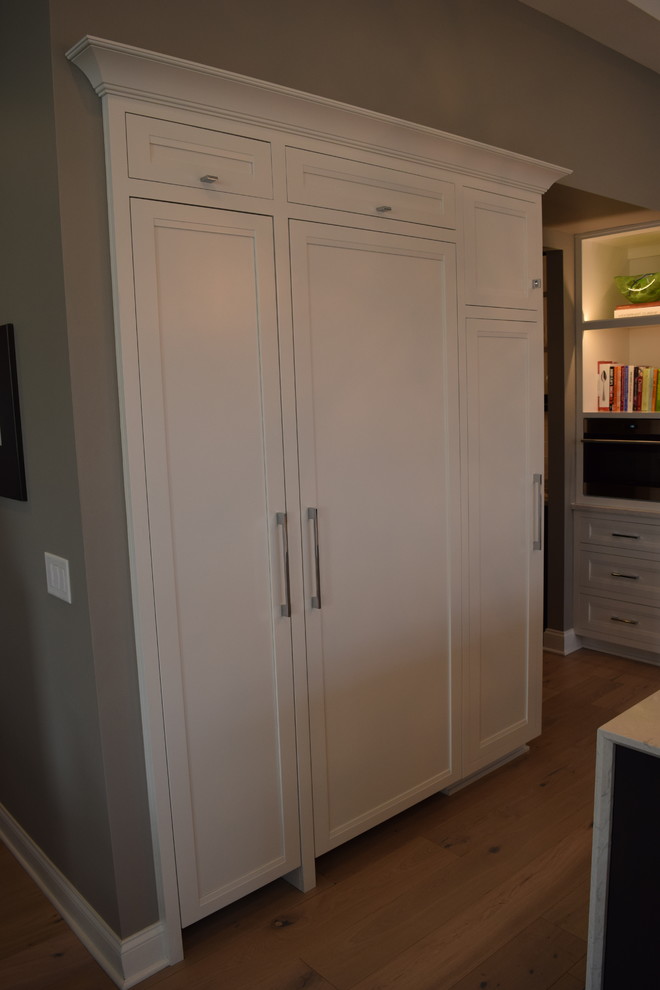 Large transitional l-shaped light wood floor and multicolored floor eat-in kitchen photo in Chicago with beaded inset cabinets, white cabinets, quartz countertops, black backsplash, ceramic backsplash, stainless steel appliances and an island