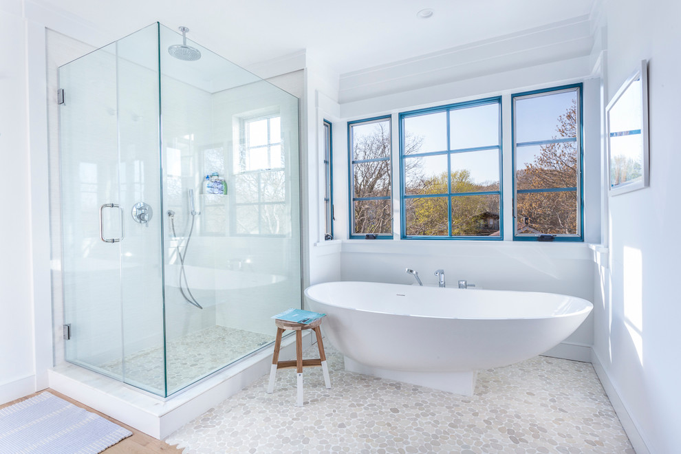 This is an example of a beach style master bathroom in New York with a freestanding tub, a corner shower, pebble tile, white walls, open cabinets, medium wood cabinets, gray tile, white tile, medium hardwood floors, an undermount sink, engineered quartz benchtops and a hinged shower door.