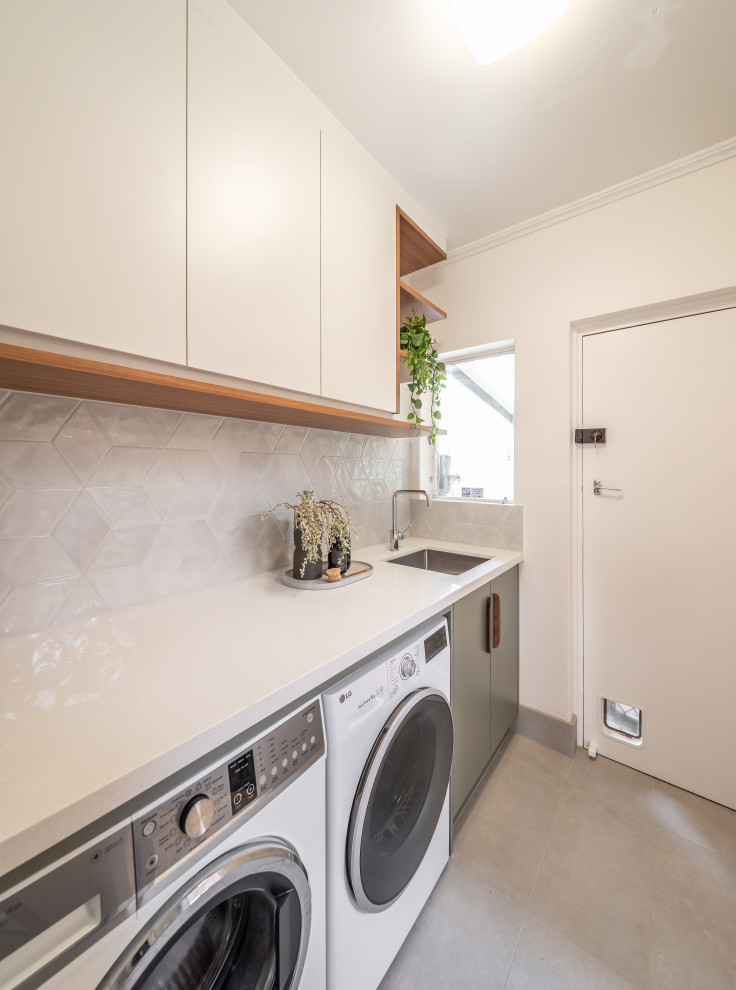 Inspiration for a small contemporary single-wall dedicated laundry room in Adelaide with an undermount sink, flat-panel cabinets, green cabinets, quartz benchtops, grey splashback, porcelain splashback, white walls, ceramic floors, a side-by-side washer and dryer, grey floor and white benchtop.