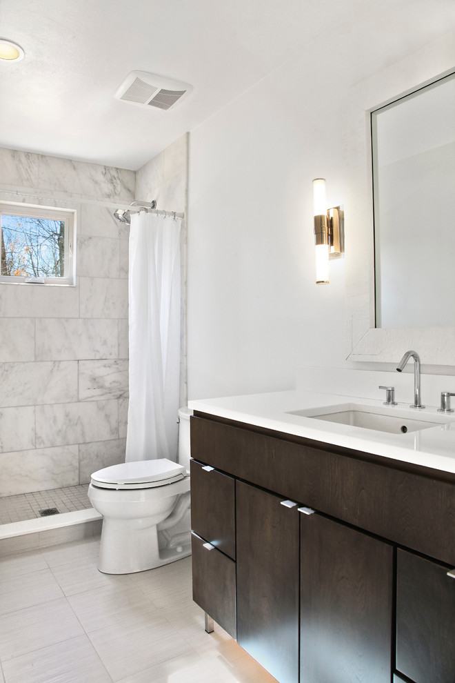 This is an example of a mid-sized transitional 3/4 bathroom in New York with flat-panel cabinets, dark wood cabinets, an alcove shower, a two-piece toilet, white tile, marble, white walls, porcelain floors, an undermount sink, solid surface benchtops, beige floor, a shower curtain and white benchtops.