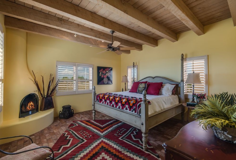 This is an example of a mid-sized master bedroom in Albuquerque with yellow walls, brick floors, a corner fireplace, a plaster fireplace surround and brown floor.
