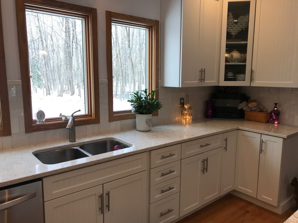 Mid-sized transitional u-shaped medium tone wood floor kitchen photo with an undermount sink, shaker cabinets, white cabinets, quartz countertops, white backsplash, ceramic backsplash, stainless steel appliances, an island and white countertops