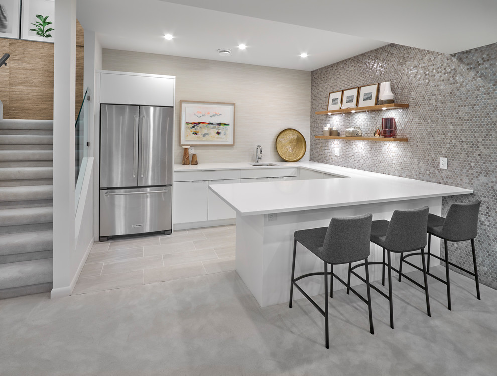 Photo of a contemporary u-shaped seated home bar in Edmonton with an undermount sink, flat-panel cabinets, white cabinets, grey splashback, mosaic tile splashback, grey floor and white benchtop.