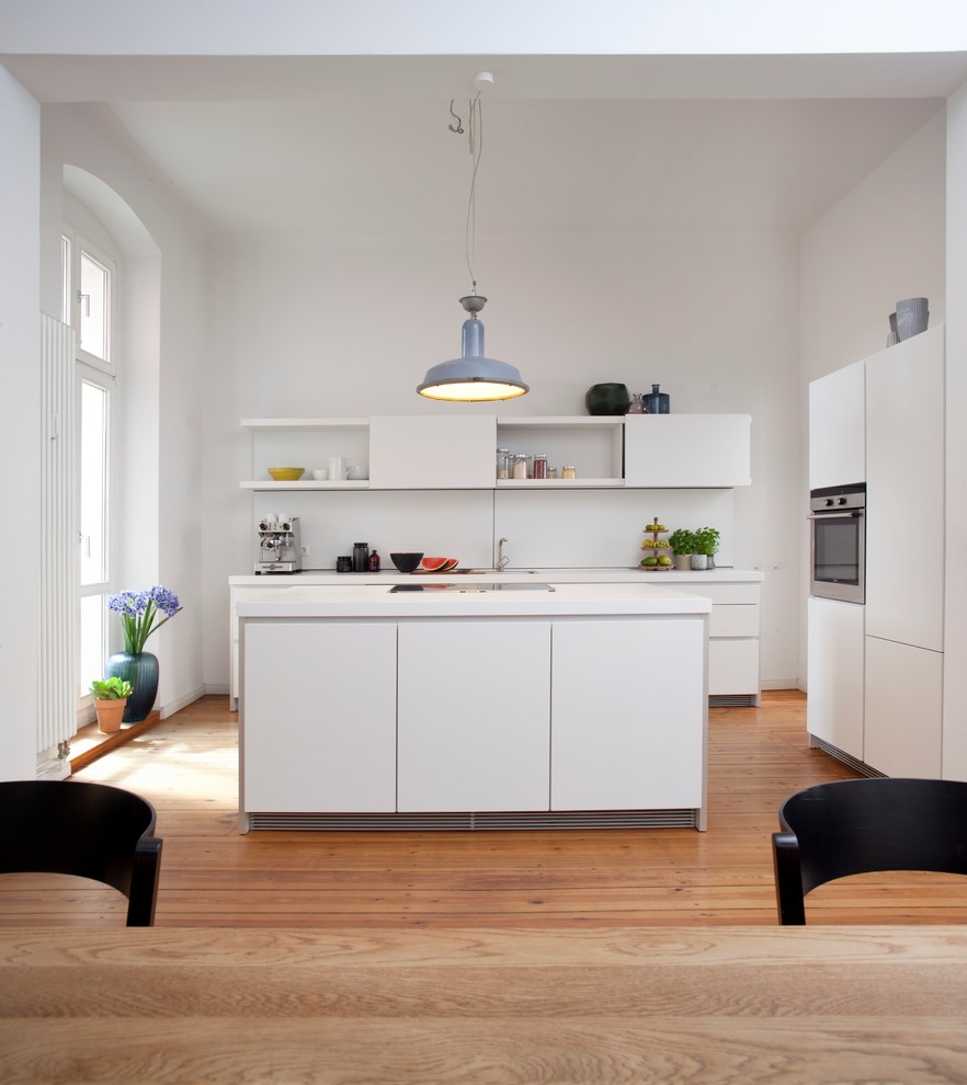Inspiration for a large contemporary open plan kitchen in Berlin with a drop-in sink, flat-panel cabinets, white cabinets, white splashback, stainless steel appliances, medium hardwood floors and with island.