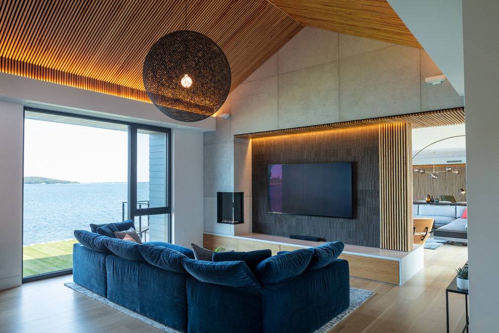 Пример оригинального дизайна: большая гостиная комната в современном стиле с белыми стенами, светлым паркетным полом, угловым камином, фасадом камина из бетона, телевизором на стене, бежевым полом, сводчатым потолком, деревянными стенами и синим диваном