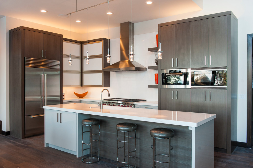 This is an example of a mid-sized modern l-shaped eat-in kitchen in Phoenix with flat-panel cabinets, grey cabinets, stainless steel appliances, with island, an undermount sink, quartz benchtops, white splashback, medium hardwood floors and brown floor.