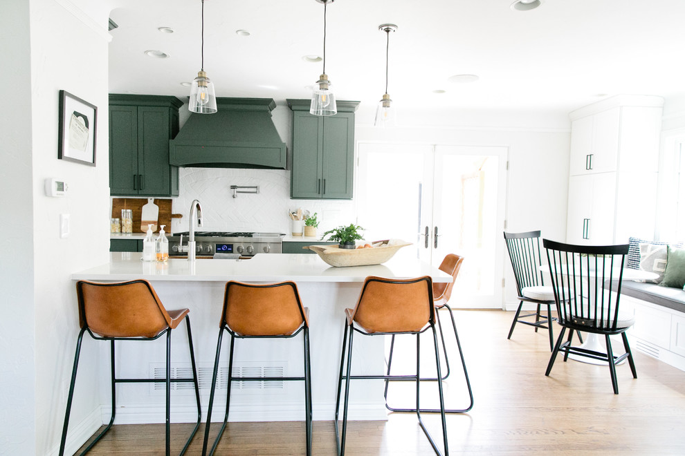 Eat-in kitchen - mid-sized transitional galley medium tone wood floor and brown floor eat-in kitchen idea in Denver with a farmhouse sink, shaker cabinets, green cabinets, quartz countertops, white backsplash, brick backsplash, stainless steel appliances, a peninsula and white countertops
