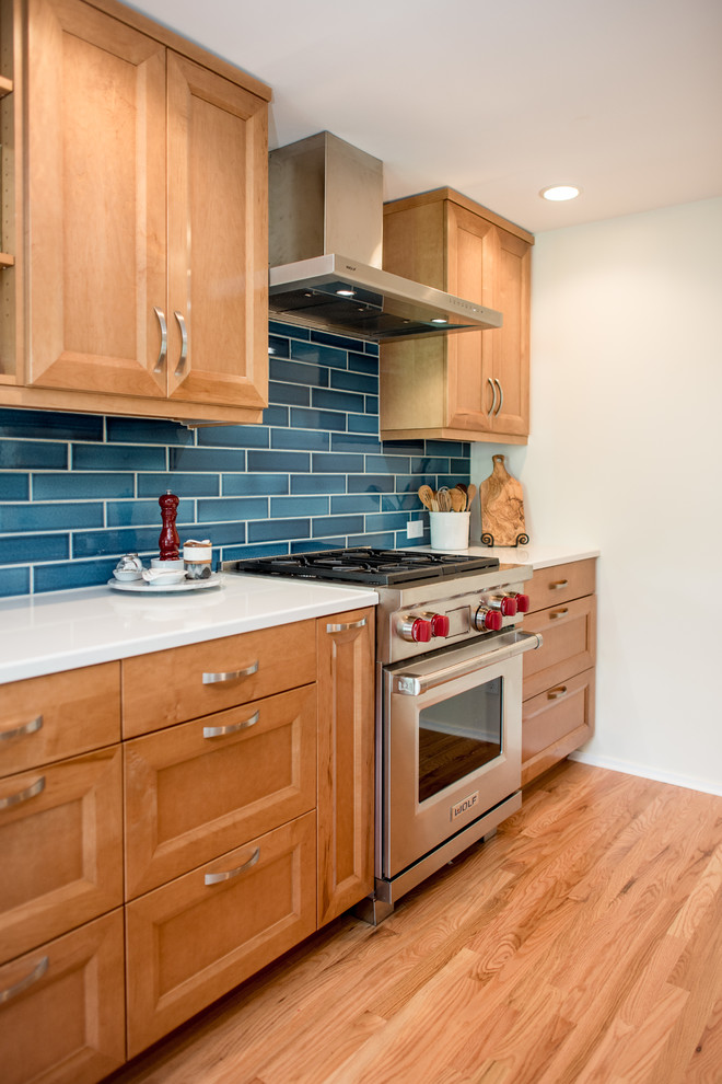 This is an example of a transitional galley kitchen in Seattle with recessed-panel cabinets, light wood cabinets, quartz benchtops, blue splashback, porcelain splashback, stainless steel appliances, light hardwood floors, no island, beige floor and white benchtop.