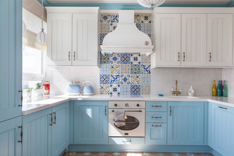 Mid-sized mediterranean u-shaped separate kitchen in Moscow with solid surface benchtops, multi-coloured splashback, ceramic splashback, white appliances, ceramic floors, no island, multi-coloured floor, white benchtop, recessed-panel cabinets, blue cabinets and an integrated sink.