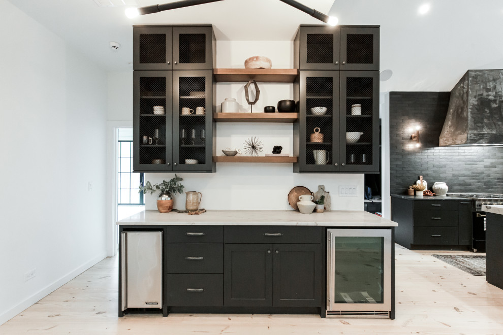 Inspiration for a large contemporary l-shaped eat-in kitchen in Atlanta with a farmhouse sink, flat-panel cabinets, black cabinets, quartzite benchtops, black splashback, subway tile splashback, black appliances, light hardwood floors, with island, beige floor, white benchtop and vaulted.