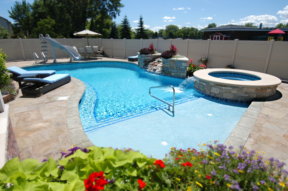 This is an example of a mid-sized beach style backyard custom-shaped natural pool in Chicago with a hot tub and natural stone pavers.