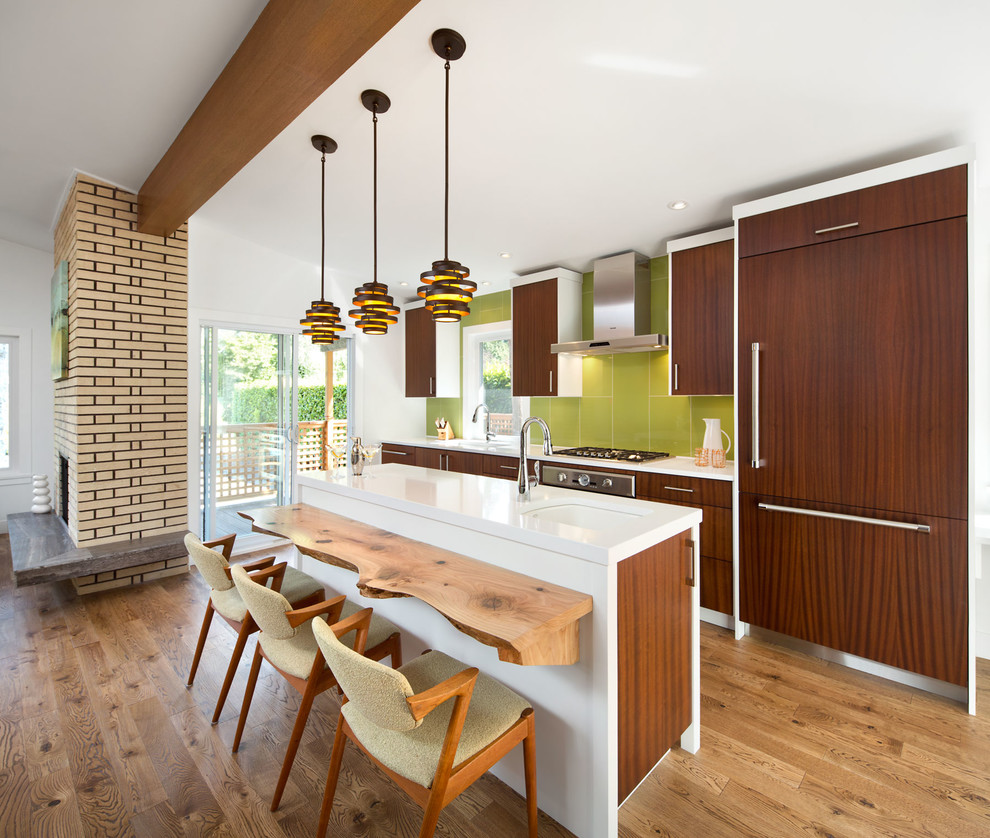 Photo of a midcentury galley open plan kitchen in Vancouver with an undermount sink, quartz benchtops, green splashback, panelled appliances, flat-panel cabinets, medium hardwood floors, with island and medium wood cabinets.