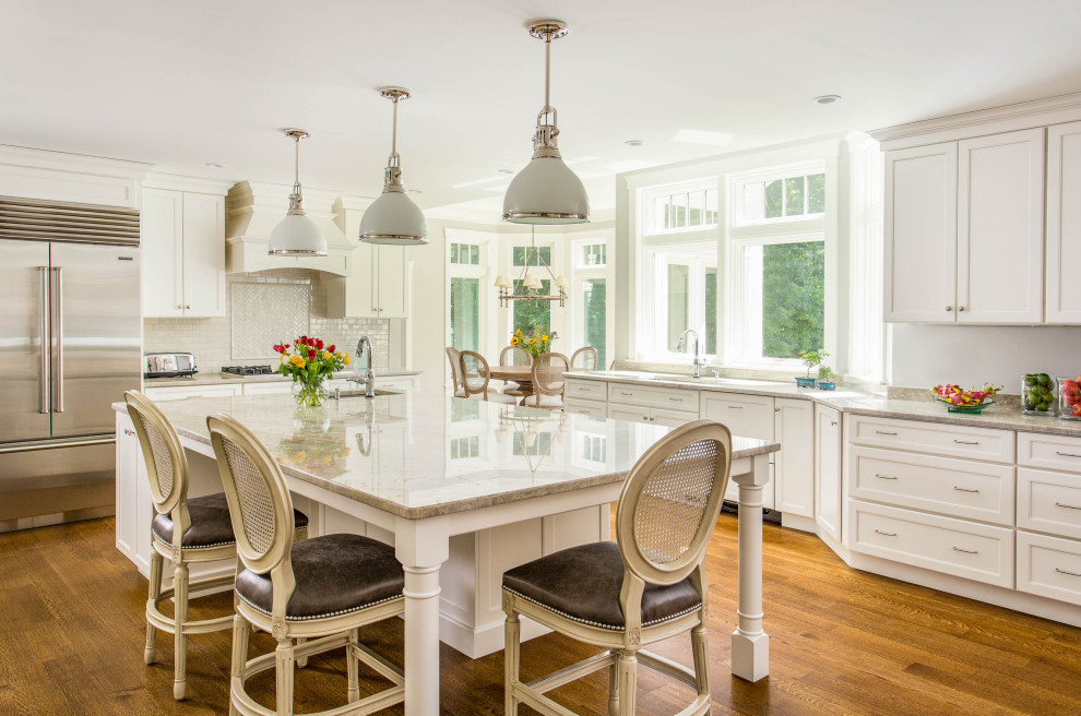 Photo of a large traditional l-shaped eat-in kitchen in Boston with white cabinets, quartzite benchtops, white splashback, porcelain splashback, stainless steel appliances, medium hardwood floors, with island, beige benchtop, an undermount sink, shaker cabinets and brown floor.