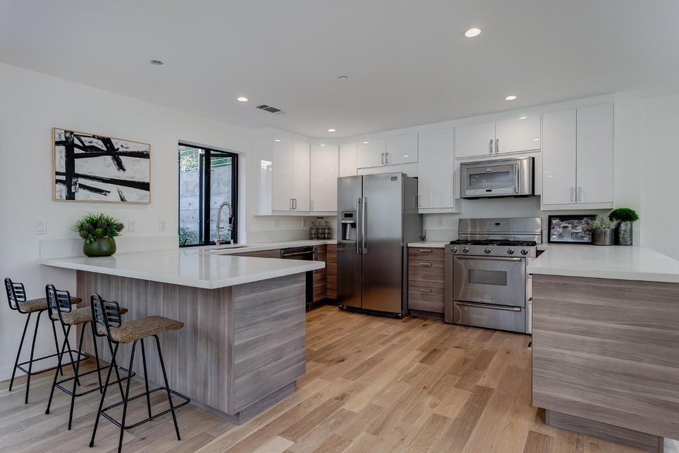 Inspiration for a mid-sized contemporary u-shaped open plan kitchen in Los Angeles with flat-panel cabinets, medium wood cabinets, panelled appliances, light hardwood floors, a peninsula, a single-bowl sink, quartzite benchtops, white splashback and subway tile splashback.
