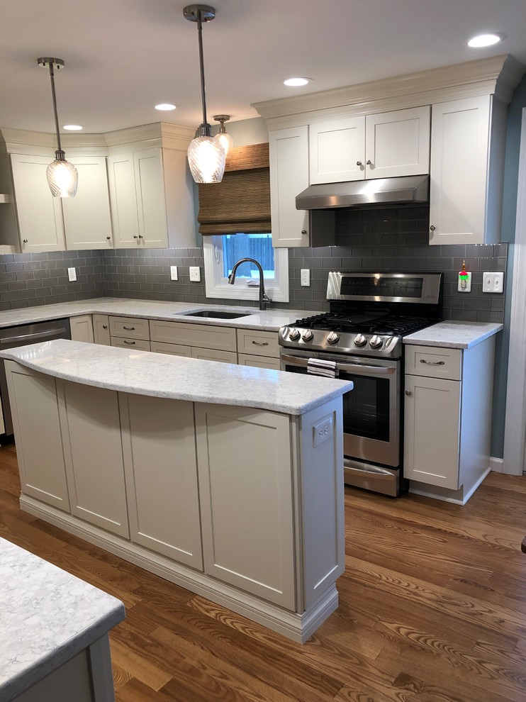 Inspiration for a large transitional l-shaped eat-in kitchen in New York with a double-bowl sink, shaker cabinets, white cabinets, quartz benchtops, grey splashback, subway tile splashback, stainless steel appliances, medium hardwood floors, with island, orange floor and white benchtop.
