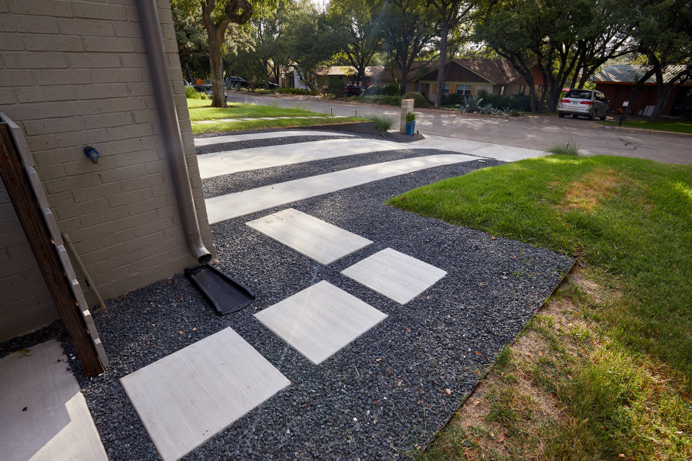 Immagine di un grande vialetto d'ingresso minimal esposto a mezz'ombra davanti casa in estate con un muro di contenimento, pavimentazioni in cemento e recinzione in metallo
