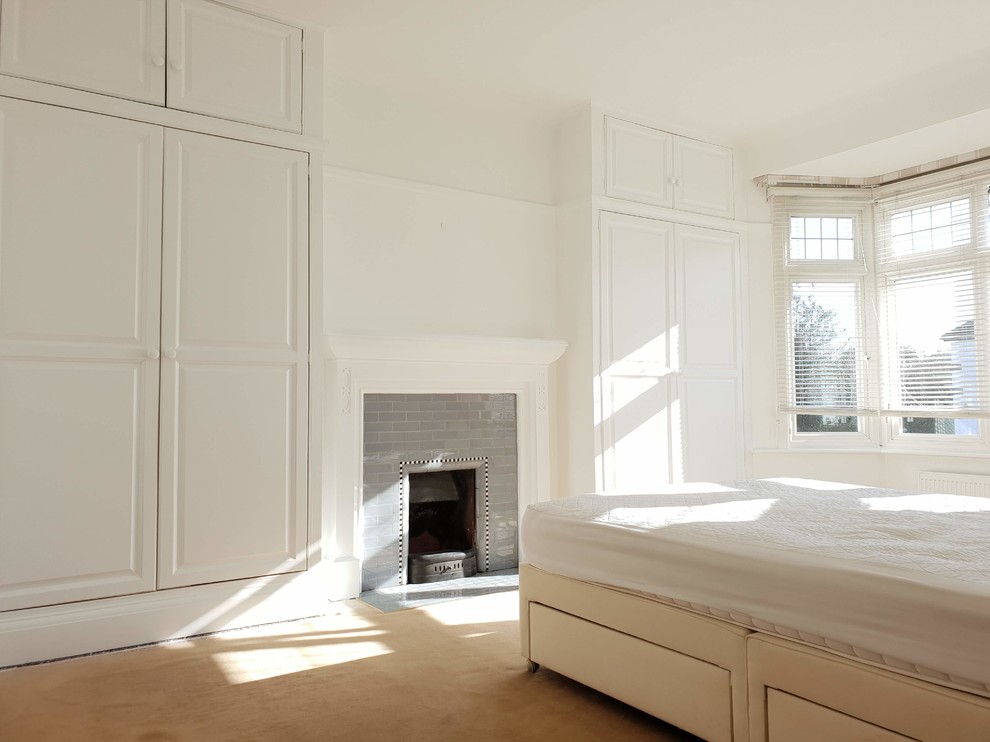 Идея дизайна: большая хозяйская спальня в классическом стиле с белыми стенами, ковровым покрытием, стандартным камином, фасадом камина из камня, бежевым полом и многоуровневым потолком