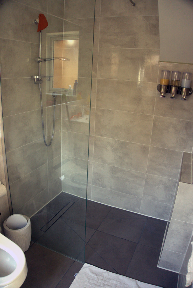 Cette image montre une salle d'eau grise et noire minimaliste de taille moyenne avec un espace douche bain, un mur gris, un sol noir, une cabine de douche à porte battante, meuble simple vasque, un carrelage gris, WC à poser, un lavabo posé, un plan de toilette en carrelage et un plan de toilette beige.