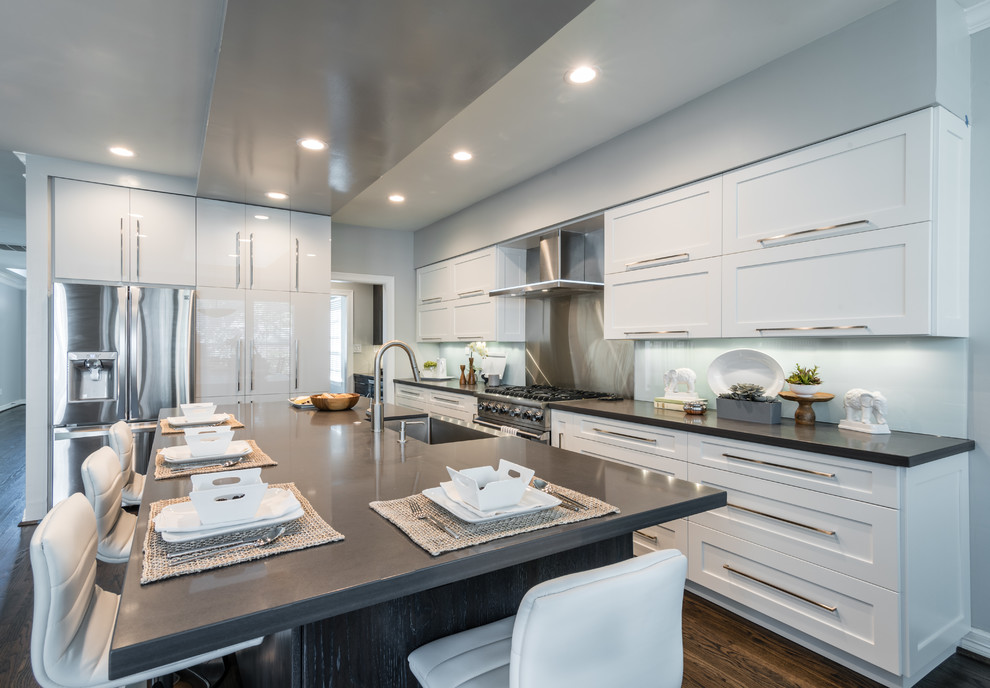 Inspiration for a mid-sized contemporary l-shaped open plan kitchen in Houston with a farmhouse sink, flat-panel cabinets, grey cabinets, quartz benchtops, grey splashback, glass sheet splashback, stainless steel appliances, dark hardwood floors and with island.