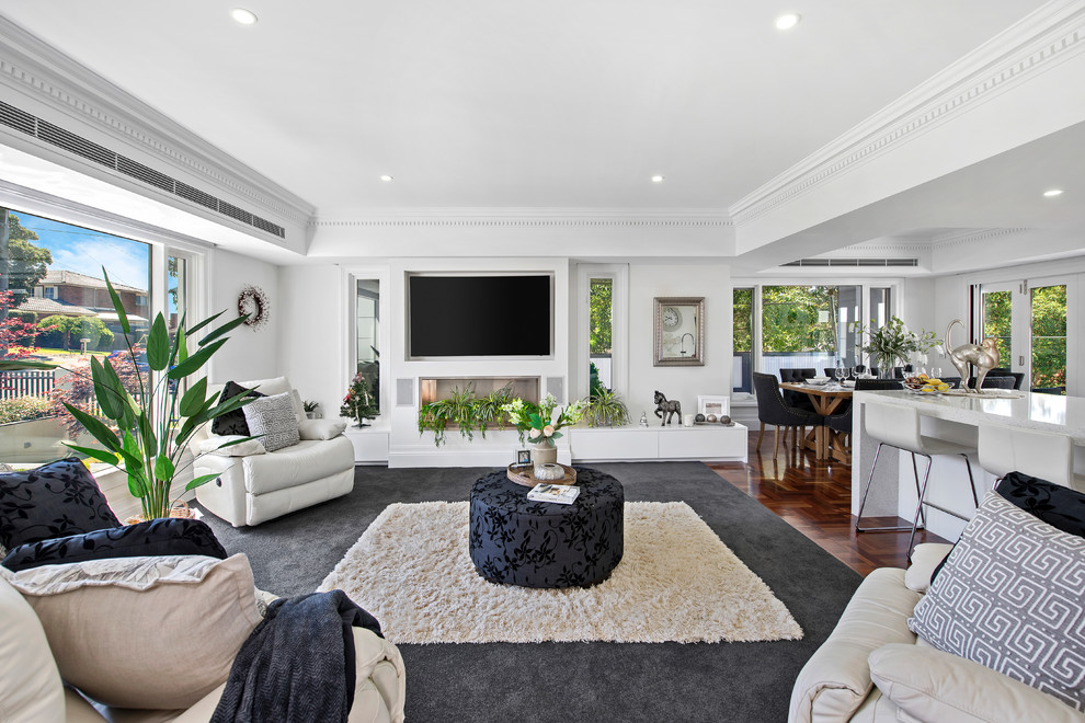 This is an example of a mid-sized contemporary open concept living room in Melbourne with white walls, carpet, a standard fireplace, a wall-mounted tv and grey floor.