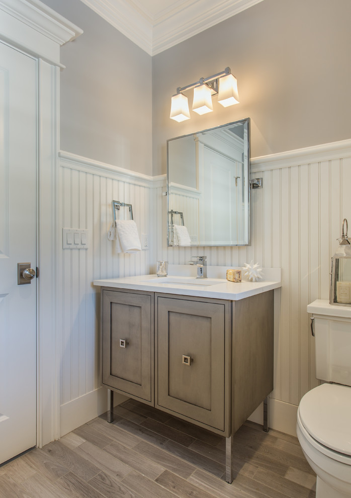 Photo of a mid-sized traditional 3/4 bathroom in Boston with grey walls, light hardwood floors, shaker cabinets, distressed cabinets, a one-piece toilet, solid surface benchtops, an undermount sink and brown floor.