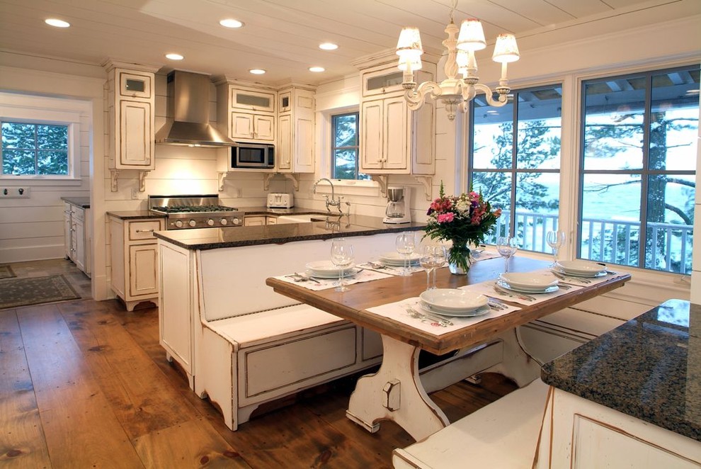 Design ideas for a mid-sized beach style u-shaped eat-in kitchen in Grand Rapids with a farmhouse sink, recessed-panel cabinets, distressed cabinets, solid surface benchtops, white splashback, timber splashback, stainless steel appliances, dark hardwood floors, no island and brown floor.
