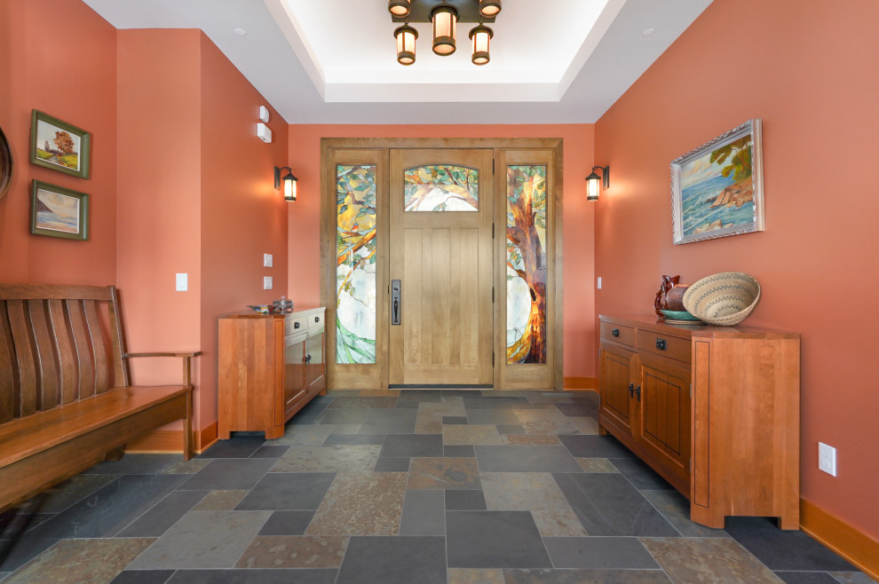 This is an example of a mid-sized arts and crafts foyer in Other with orange walls, slate floors, a single front door, a medium wood front door and recessed.